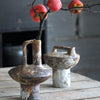 A vintage handcrafted ceramic vase holds a branch with red berries against a dark background.