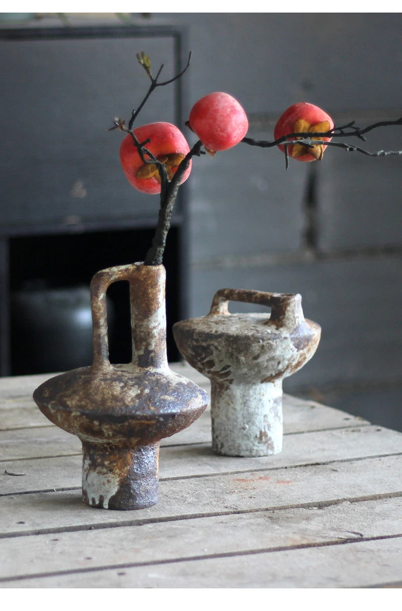 A vintage handcrafted ceramic vase holds a branch with red berries against a dark background.