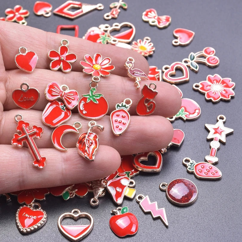 A hand holds an assortment of gold-tone enamel charms featuring hearts, flowers, strawberries, and stars for jewelry making.