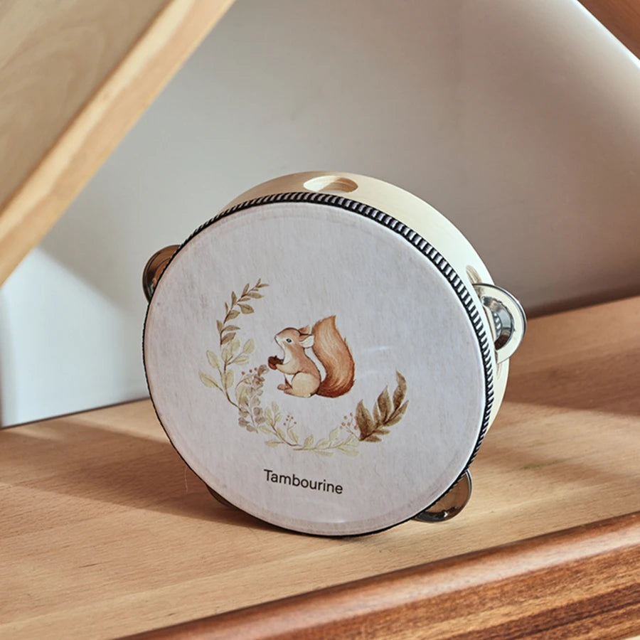 A round wooden tambourine with a light beige surface and decorative floral elements resting on a wooden surface.