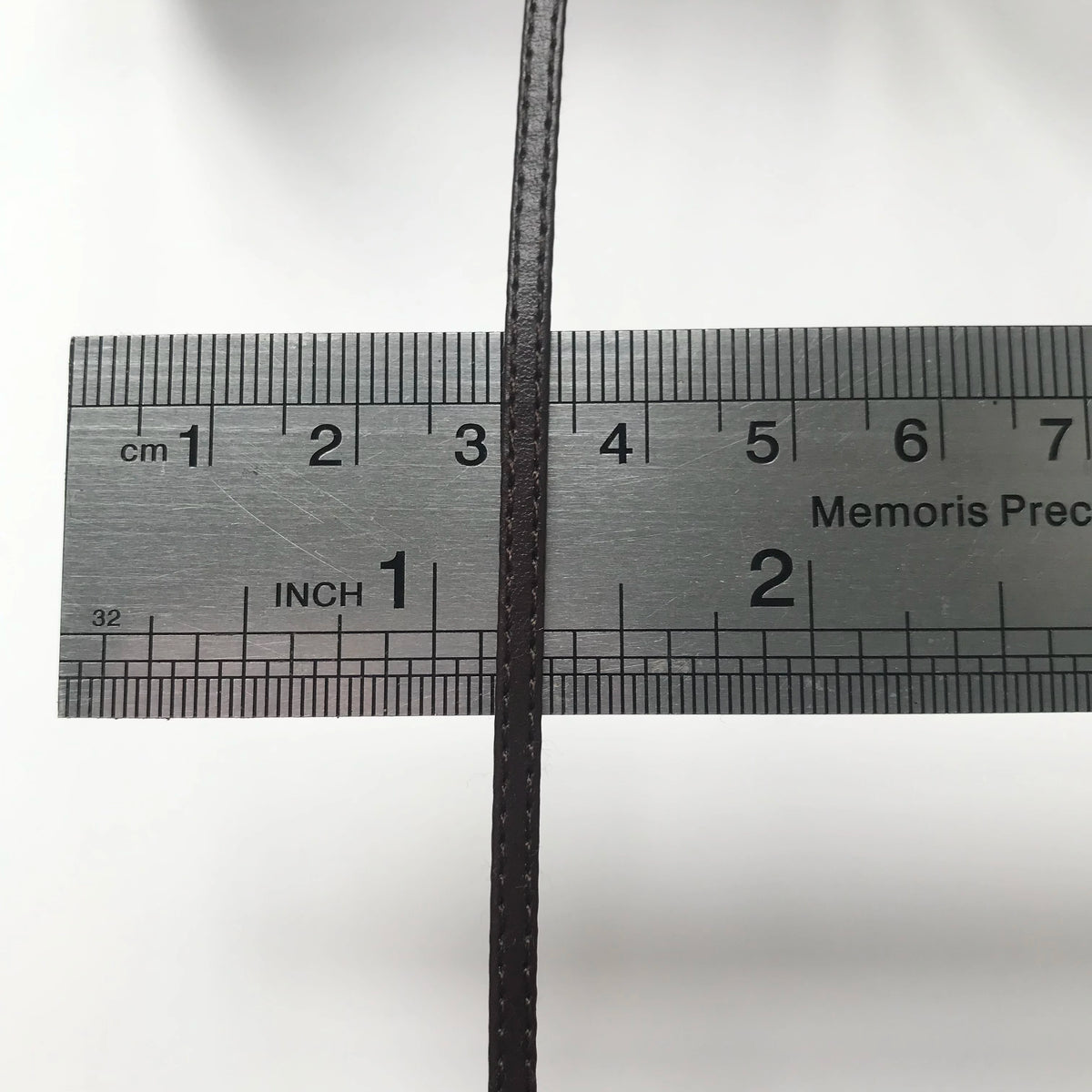 Schwarzes Maßband mit Zentimeter- und Zollmarkierungen, kreuzförmig durch einen dünnen schwarzen Stab.