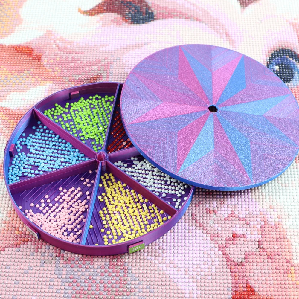 A purple rotating diamond painting storage tray organizer filled with colorful beads on a pink textured surface.