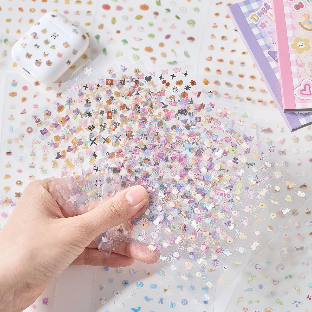 A hand is holding a clear sheet of die-cut stickers, showing a colorful assortment of cute cartoon stickers.