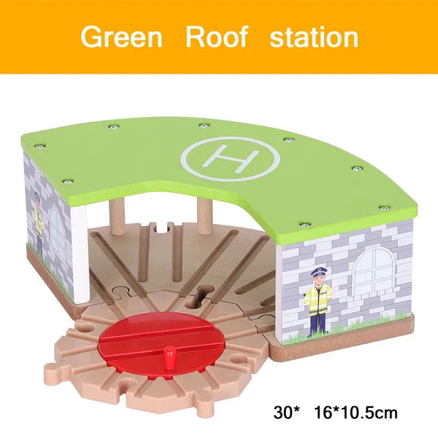 A wooden train track accessory set featuring a green roof station model with an airport or gas station scene.