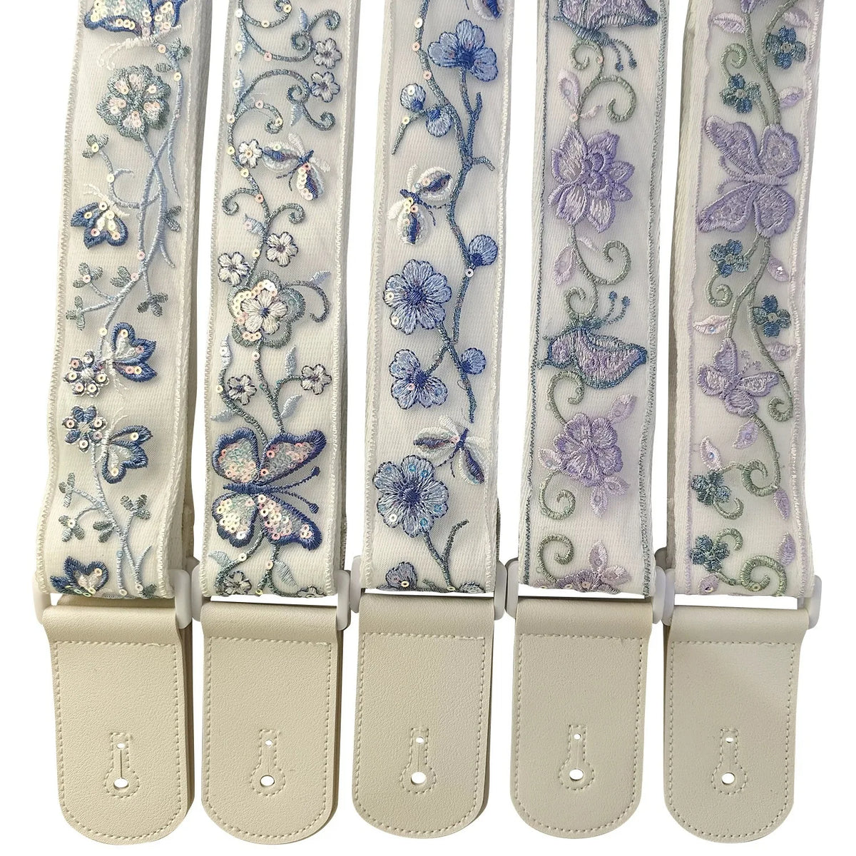 A set of light-colored woven guitar straps with floral embroidery and leather accents.