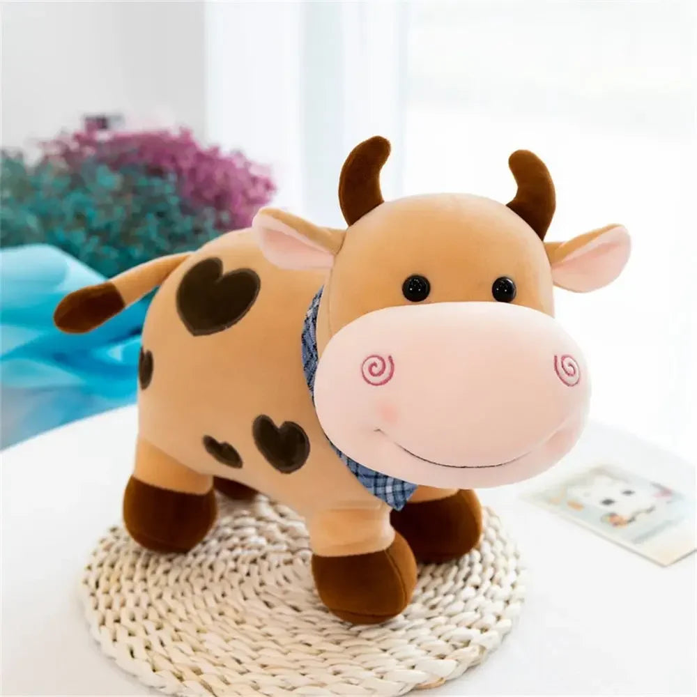 A soft, brown cow plush toy with black heart markings and pink nose, sitting on a woven surface.