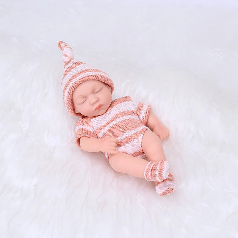 A realistic soft vinyl baby doll wearing a pink striped outfit and matching hat, lying on white fluffy fabric.