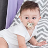 A baby wearing a personalized pacifier with a crown design resting on a gray and white striped cloth.