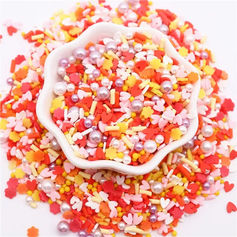 A pile of colorful polymer clay sprinkles mix featuring red, orange, pink, and yellow heart shapes and pearl accents.