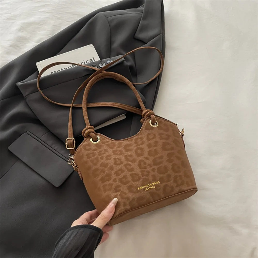 A brown leopard print canvas tote bag with leather handles is shown next to a gray blazer.