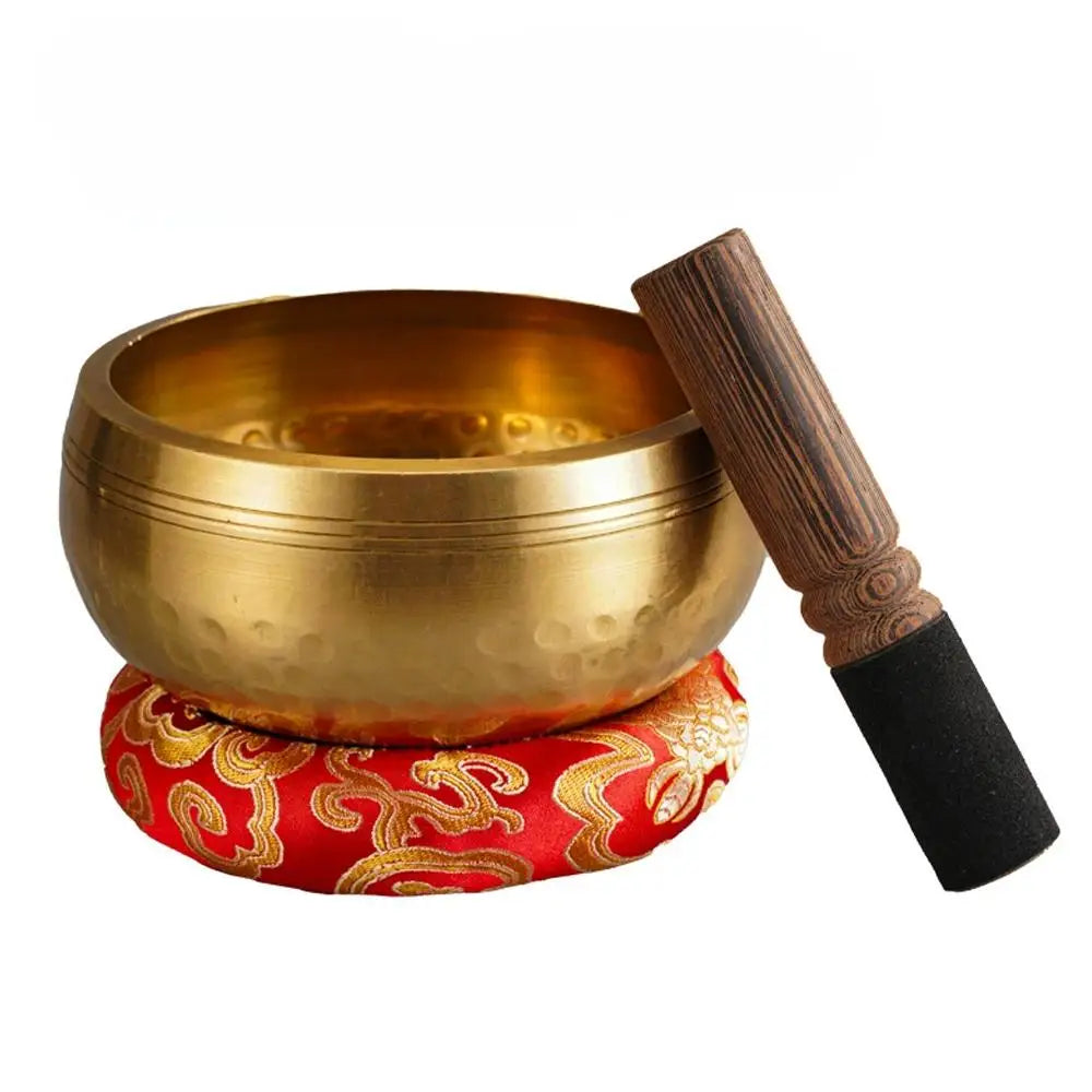 A brass singing bowl and a wooden mallet are displayed on a red fabric cushion.
