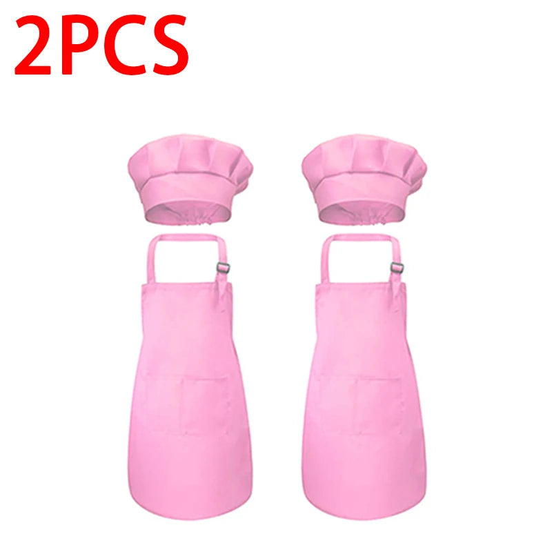 A pair of pink kids' chef apron and hat set displayed side by side.