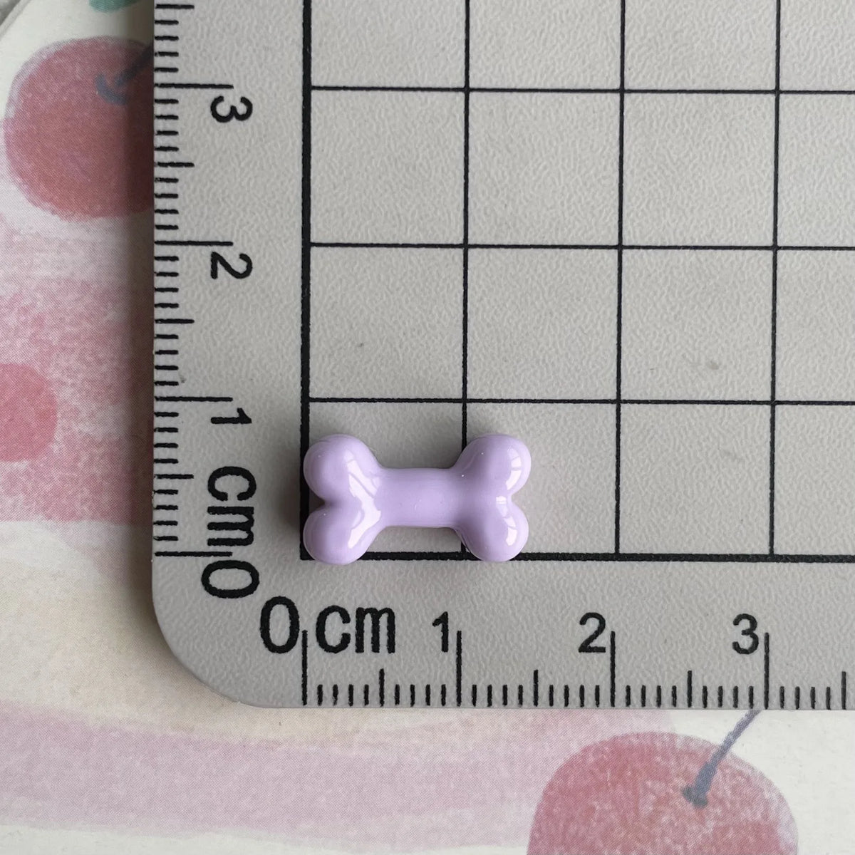 A small, light purple resin bone charm is placed on a ruler marked in centimeters.