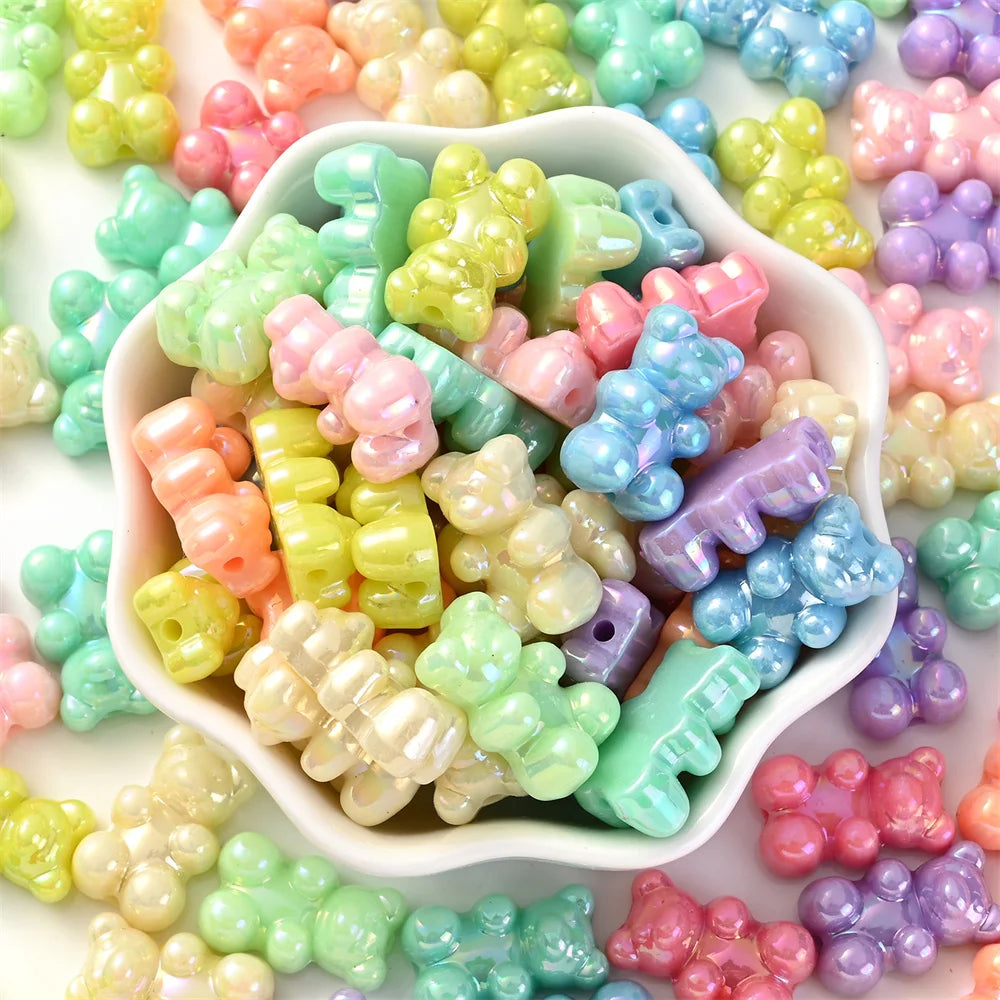 A close-up of various pastel bear-shaped acrylic craft beads in shades of pink, green, yellow, and blue scattered on a white 