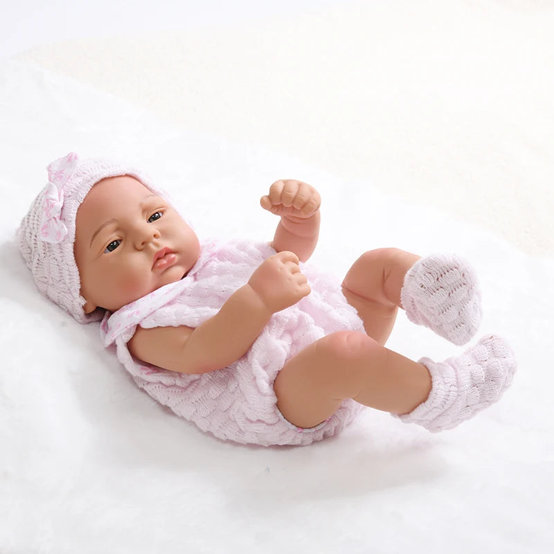 A lifelike vinyl reborn doll with a pink outfit and matching hat lying on a white surface.