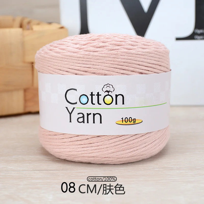 A ball of pink cotton yarn labeled as Cotton Yarn 100g, shown on a wooden surface.