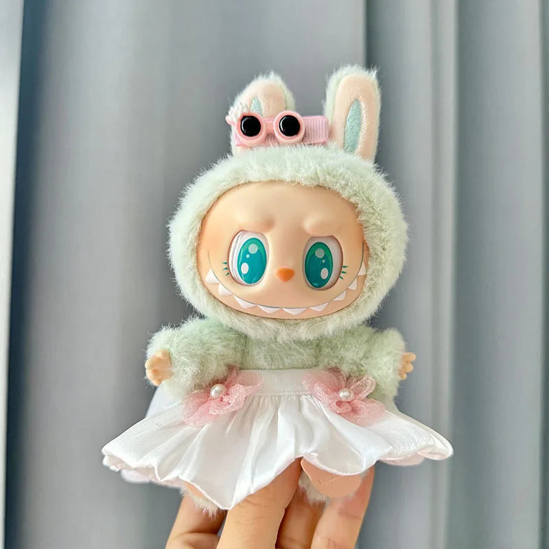A cute doll wearing a light green fuzzy outfit and a white ruffled skirt with pink flowers.