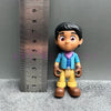 A playful cartoon PVC figurine of a boy with dark hair and large eyes, dressed in blue and yellow clothing.