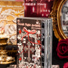 A stack of Occult Night Archive die-cut sticker sheets with red and black designs displayed next to a gold candle and rose.