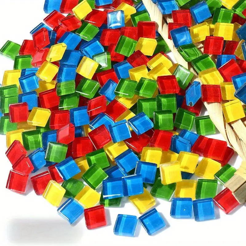 A pile of colorful crystal glass mosaic tiles in various shades of red, green, yellow, and blue mixed with natural straw.