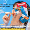 A hand is blowing a white cigarette-shaped bubble toy, next to a box of filter cigarettes.