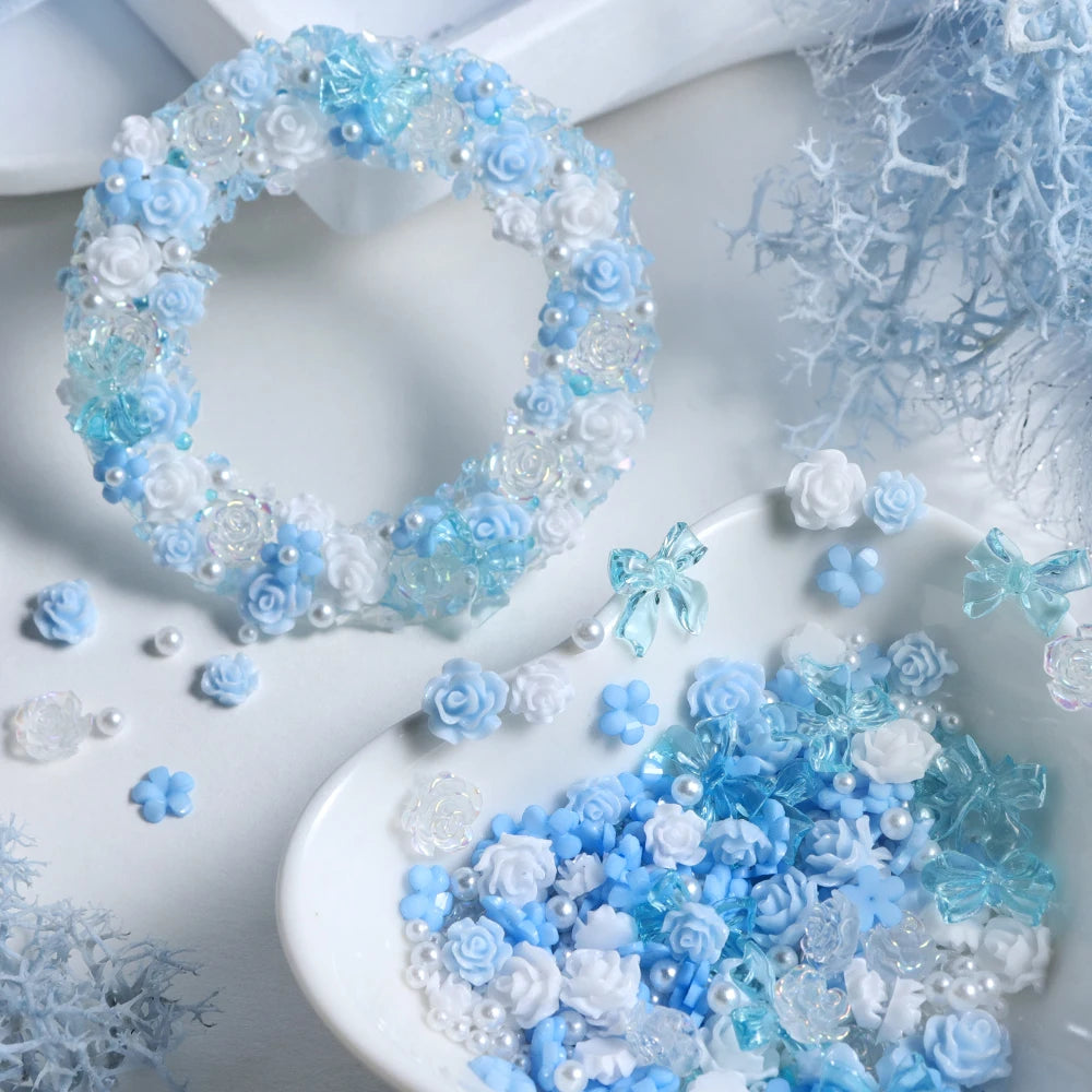 A close-up of blue and white camellia bowknot resin shakers and floral decorations on a white surface.