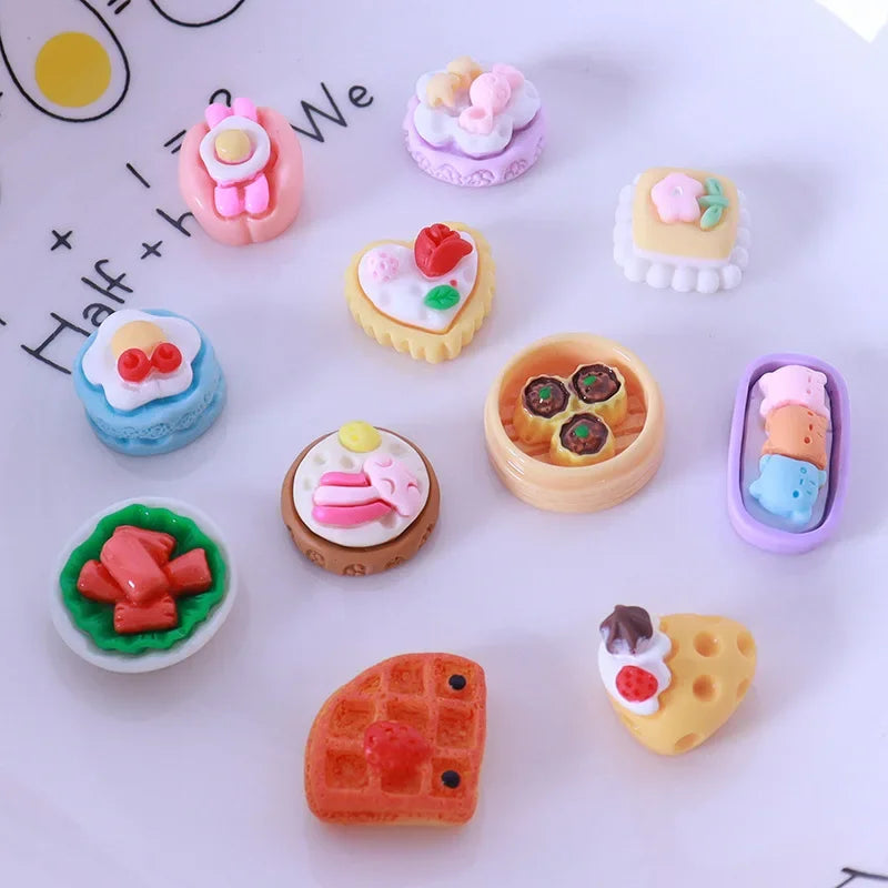 A collection of miniature dollhouse-themed snack foods including cakes, pastries, and candies arranged on a white surface.