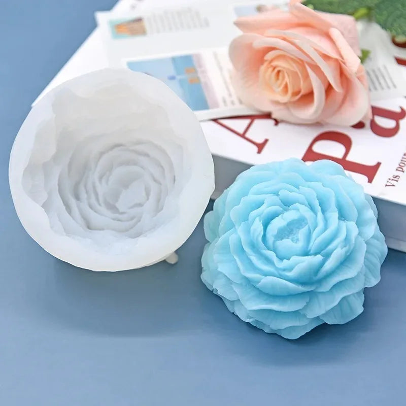 A light blue silicone mold shaped like a peony flower is shown next to a pink rose and a book.