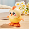 A yellow wind-up chick toy with orange accents sitting on a wooden surface next to white and yellow flowers.
