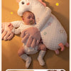 A baby is resting on a white unicorn plush pillow with pink accents and wearing pink gloves.