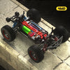 A high-speed 4WD brushless RC monster truck model with black and red components on a stone surface.