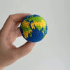A handcrafted crochet globe charm showing the continents of Earth in blue and green yarn, held in a hand.