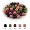 A collection of 15 hexagonal silicone beads in various shades of pink, green, and black arranged on a white plate.