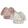 A full-sleeve waterproof baby bib with a light pink cartoon design featuring various cute animal shapes.