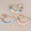 A set of wooden pacifier clips featuring silicone beads in shades of blue, white, and pink.