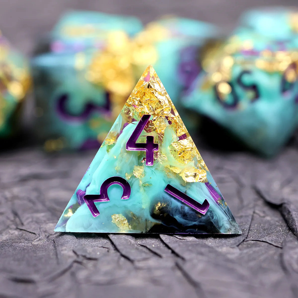 A triangular resin die with a teal and purple marbled pattern and gold accents resting on a dark surface.