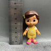 A playful cartoon PVC figurine of a girl with brown hair and yellow clothing standing next to a ruler.