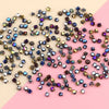 A scattered collection of iridescent crystal glass beads in various shades of purple, blue, and gold on a pink background.