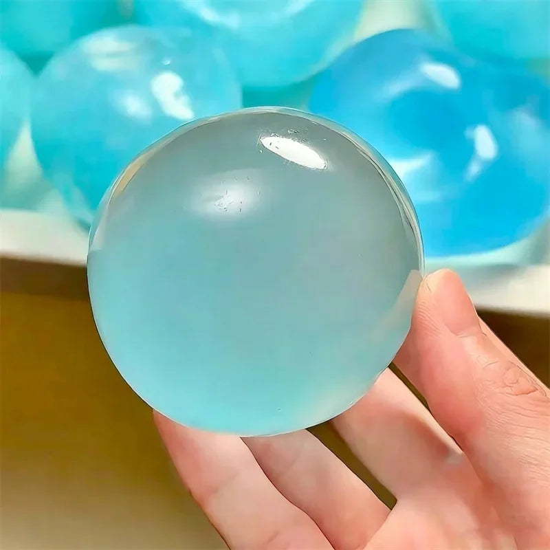 A hand holds a smooth, light blue silicone fidget ball surrounded by other similar balls.