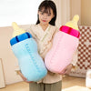 A young woman holds a pink milk bottle plush pillow with a yellow cap and a blue cap.