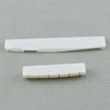 A white real bone guitar nut and bridge saddle placed on a gray surface.