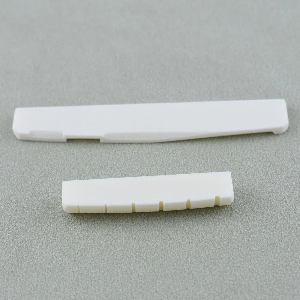 A white real bone guitar nut and bridge saddle placed on a gray surface.