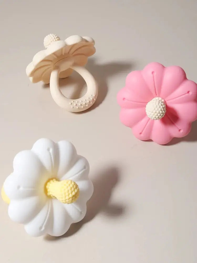 Drei Silikon-Zahnen in Form von Pilzen, Blumen und einer Margerite in Weiß und Pink.