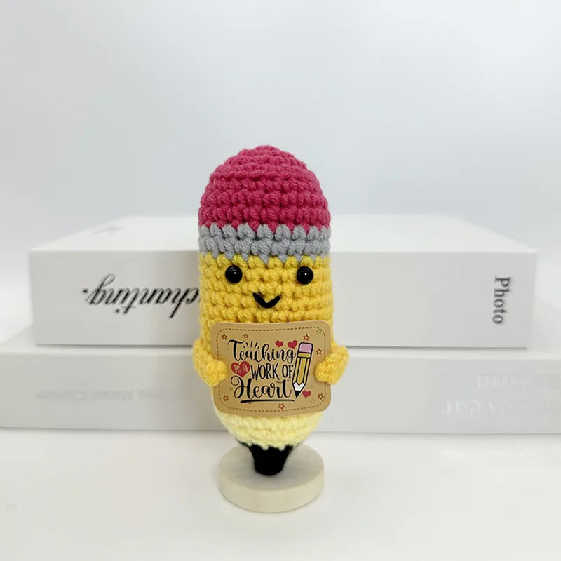 A handwoven crochet pencil ornament featuring a pink knitted cap and yellow body with a heart design.