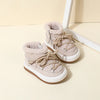 A pair of light beige baby winter snow boots with plush lining and white soles resting on a light surface.