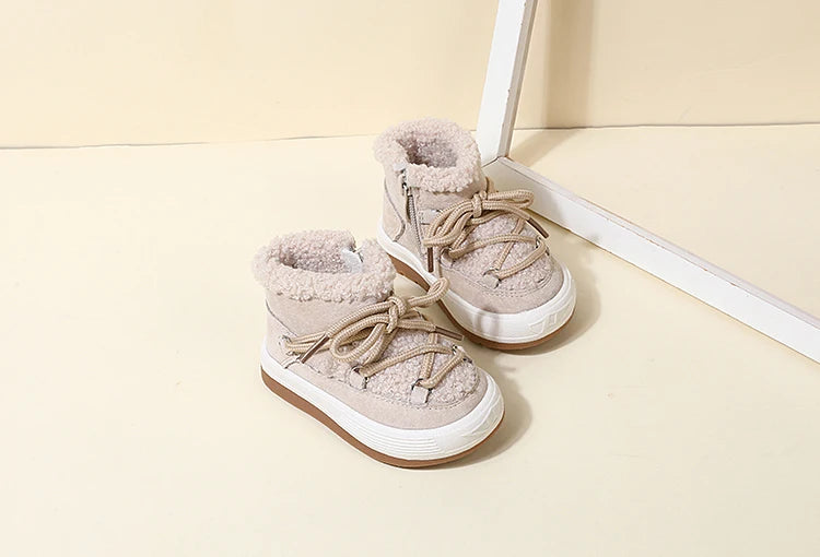 A pair of light beige baby winter snow boots with plush lining and white soles resting on a light surface.