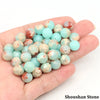 A hand holds a collection of natural stone round beads in various shades of light blue and pinkish-red.
