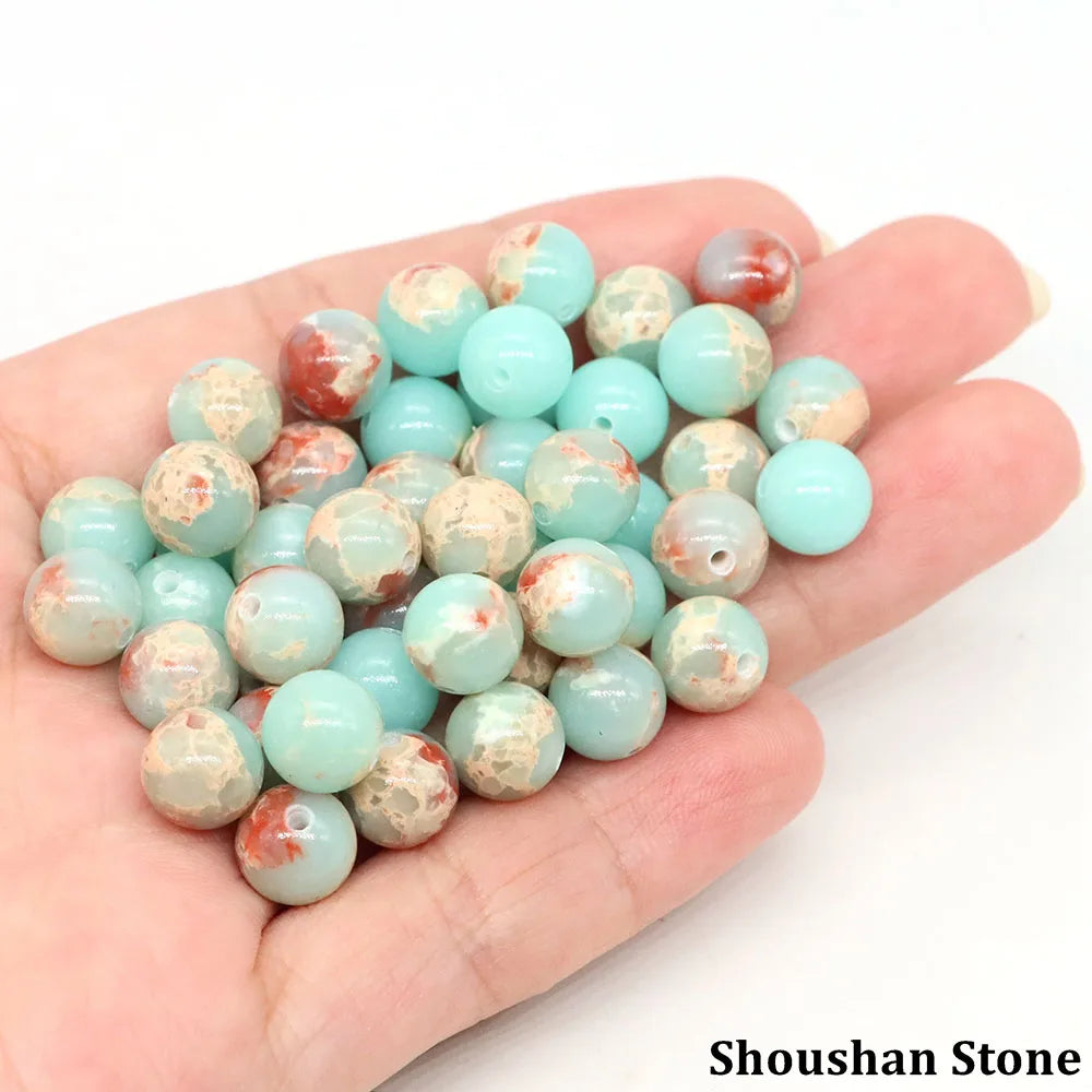 A hand holds a collection of natural stone round beads in various shades of light blue and pinkish-red.