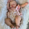 A newborn baby doll with hand-painted skin is lying peacefully in a fluffy white fur blanket.