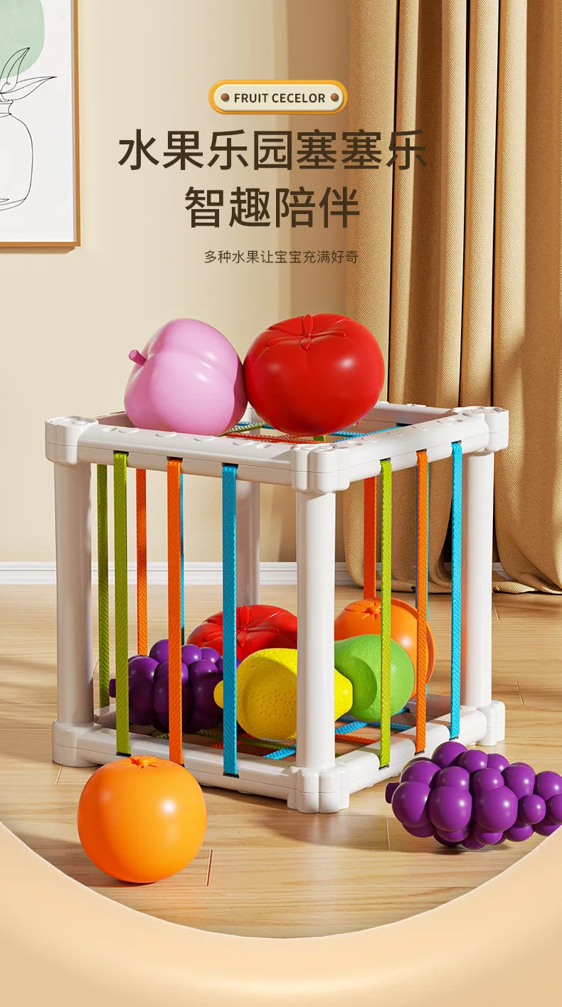 A wooden fruit shape sorter cube with various colorful fruits hanging from it, displayed on a light wood floor.